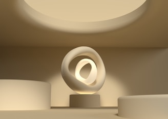 A minimalist, modern interior space featuring a smooth, sculptural object with intertwined rings illuminated by ambient lighting. The setting includes circular architectural elements and a warm, monochromatic color palette.