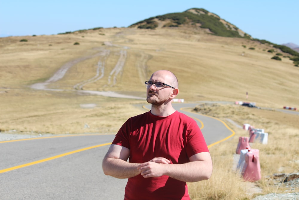 a man standing in front of a road with a hill in the background