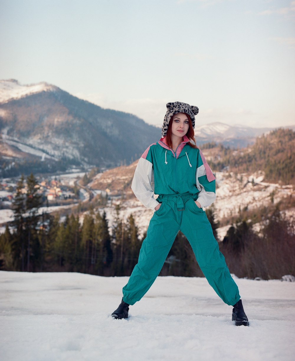 a man in a green and white outfit standing on snow with trees and mountains in the background