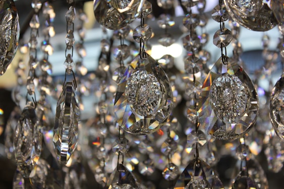 A close-up view of several hanging crystal prisms with intricate facets that catch and reflect light, creating a spectrum of colors and reflections. The crystals are elongated and drop-shaped, elegantly arranged and interconnected.