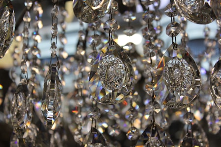 A close-up view of several hanging crystal prisms with intricate facets that catch and reflect light, creating a spectrum of colors and reflections. The crystals are elongated and drop-shaped, elegantly arranged and interconnected.