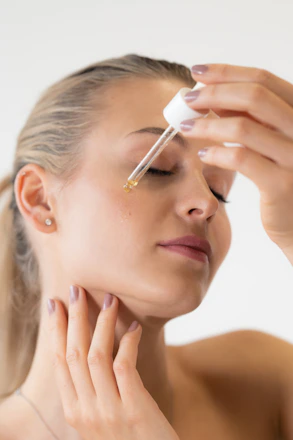 A woman applying a drop of facial serum from a glass dropper