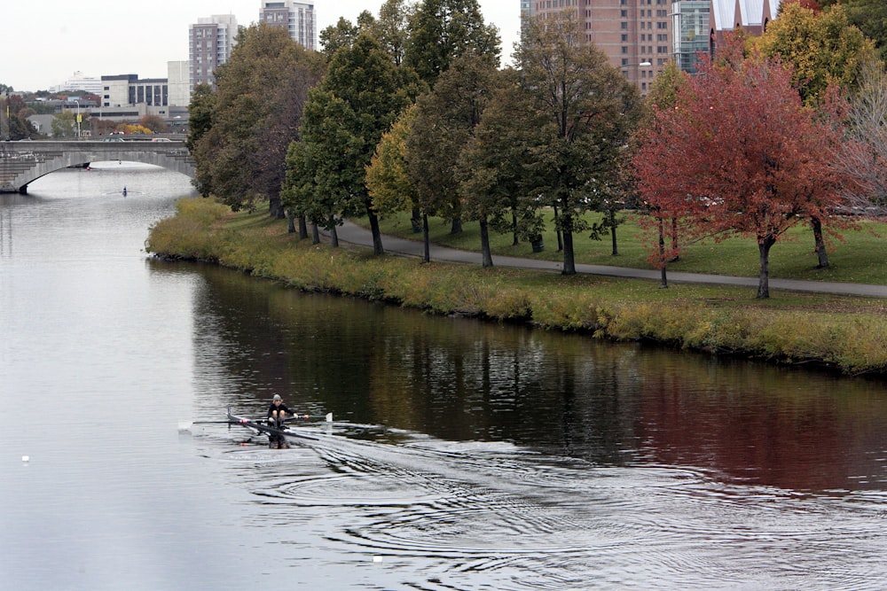 a person rowing a boat on a river with trees and buildings in the background