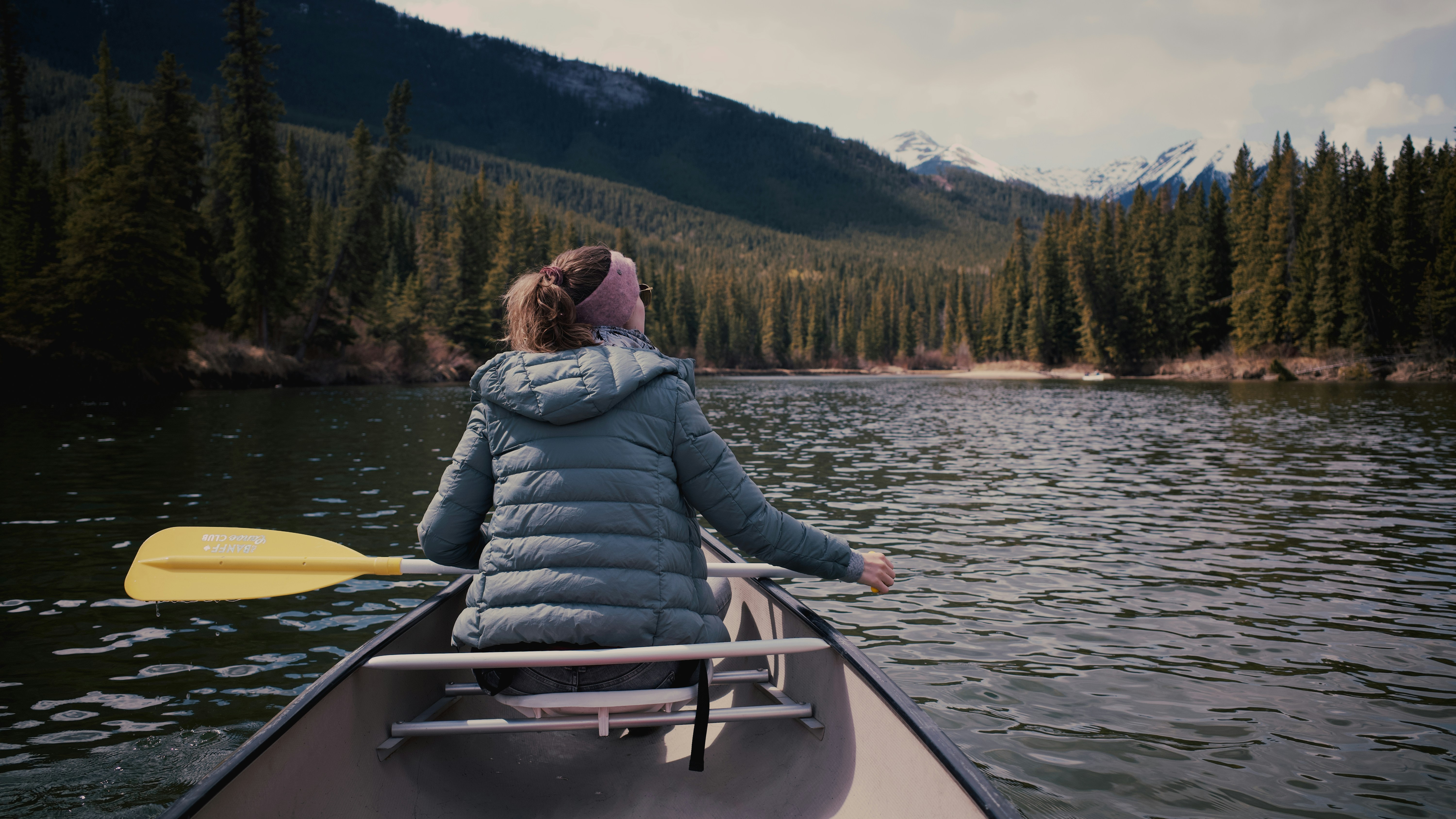 Una persona en un bote en un lago con árboles y montañas al fondo