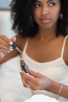 Woman gently applying rosemary hair oil to her scalp in soft natural light.