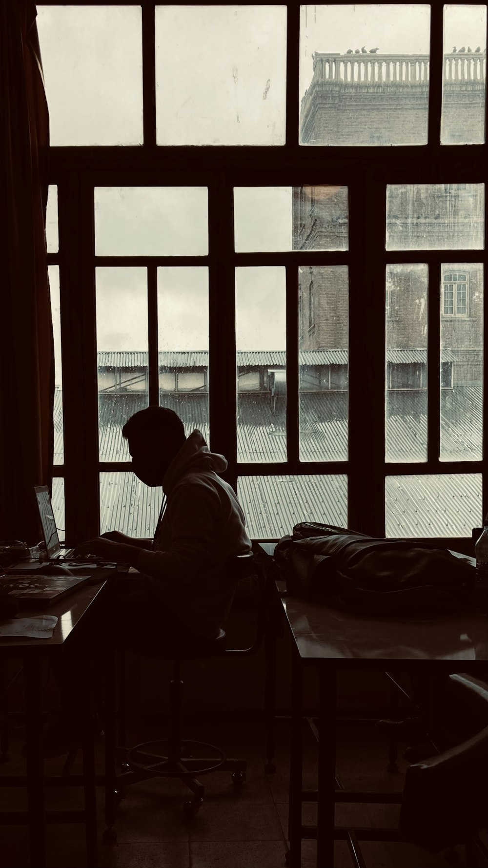 a man sitting at a desk with a laptop in front of a window