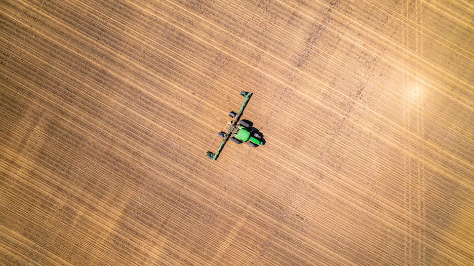 Tractor with green nozzles actively sprays large flat field in daylight under clear skies