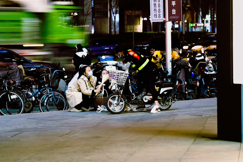 a group of people sit on a sidewalk next to some motorcycles