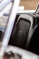 A close-up view of a car seat with black leather upholstery featuring detailed stitching and a textured center section. The surrounding frame of the car's interior is partially visible, with a soft out-of-focus effect.