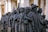 A bronze sculpture depicting a diverse group of people standing closely together. They appear to be of different cultural backgrounds, dressed in various historical and traditional clothing styles, and some hold personal belongings or wear headscarves.