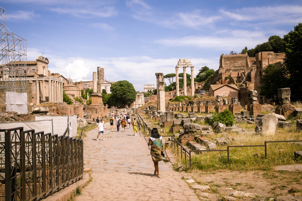 people walking on a stone path with Roman Forum in the background