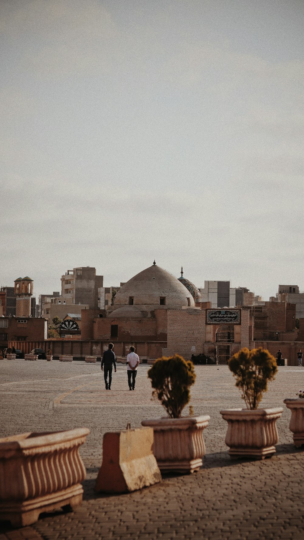 a group of people walking in a courtyard with a domed building in the background