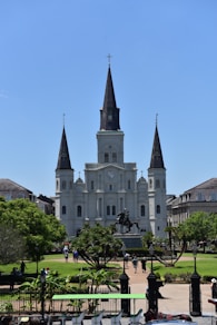 a large white building with a clock tower with St. Louis Cathedral in the background
