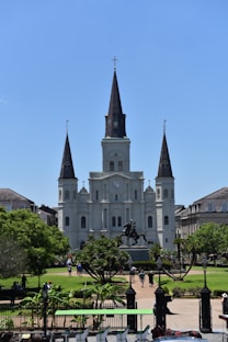 a large white building with a clock tower with St. Louis Cathedral in the background