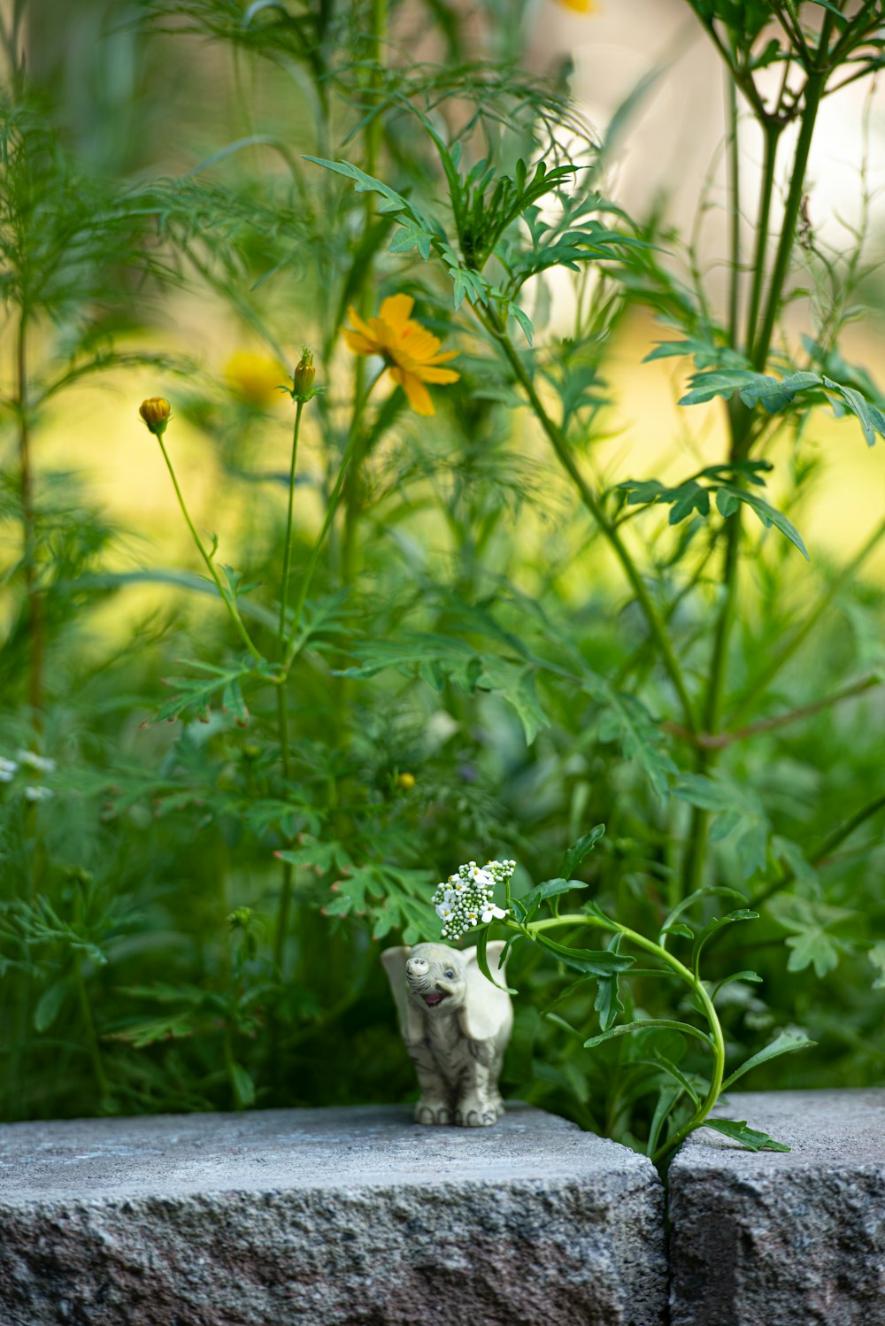 Una estatua de un gato frente a un jardín de flores