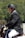 A person wearing a black riding helmet and a formal jacket sits on a horse, engaged in an equestrian activity. The background is a blurred mix of green foliage, suggesting an outdoor setting.