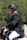 A person wearing a black riding helmet and a formal jacket sits on a horse, engaged in an equestrian activity. The background is a blurred mix of green foliage, suggesting an outdoor setting.