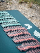 A geometric arrangement of energy bars is displayed on a blue surface. There are three distinct rows of bars, primarily in mint green and red packaging. The background features a rocky and grassy terrain.