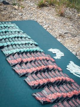A geometric arrangement of energy bars is displayed on a blue surface. There are three distinct rows of bars, primarily in mint green and red packaging. The background features a rocky and grassy terrain.