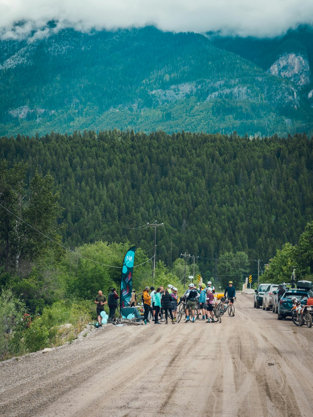 a group of people standing on a dirt road with bikes and cars