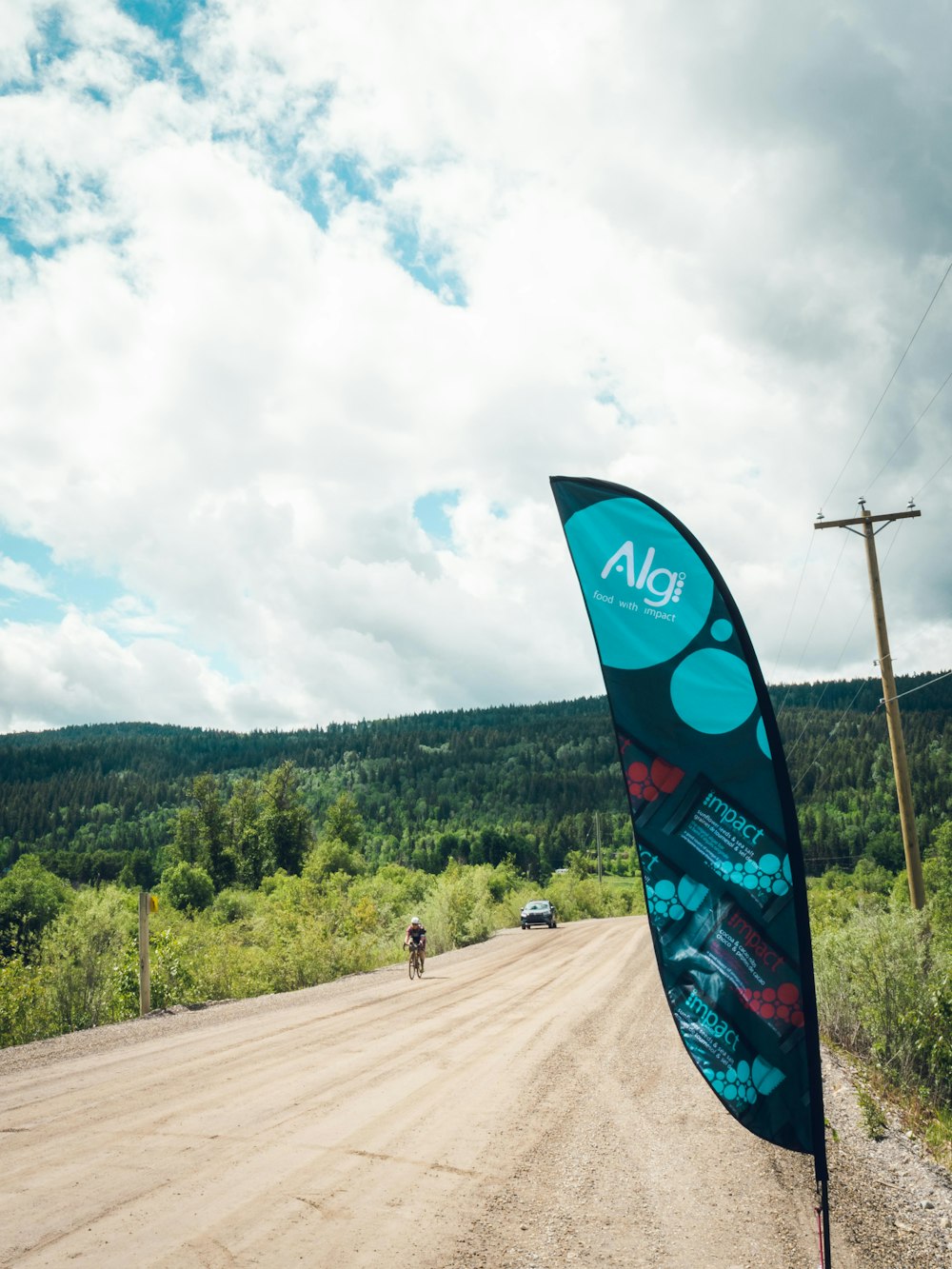 a person riding a bicycle on a dirt road with trees and a hill in the background