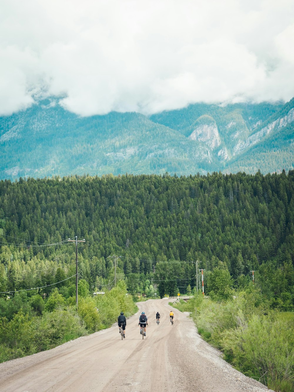 a group of people riding bikes on a dirt road in front of a mountain range