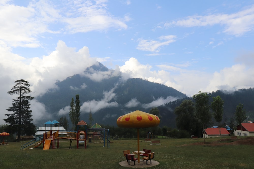 a grassy area with a few tables and umbrellas and a mountain in the background