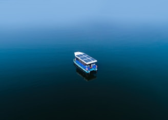 Sleek trimaran boat with hybrid sails and solar panels gliding on calm blue waters.