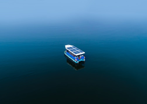 Sleek trimaran boat with hybrid sails and solar panels gliding on calm blue waters.