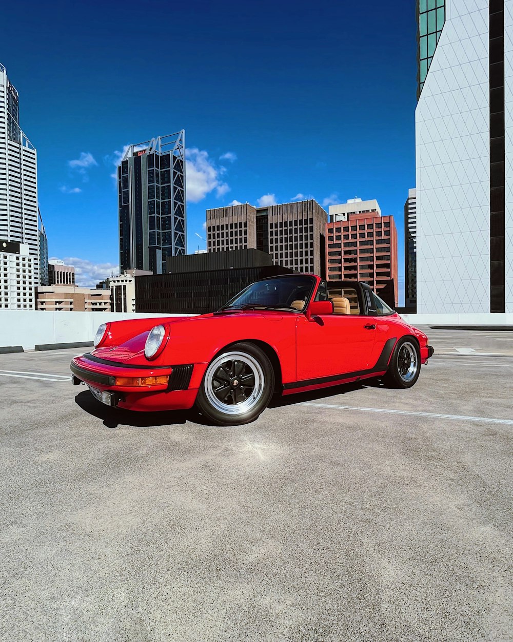 a red sports car parked in a parking lot with tall buildings in the background