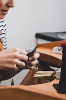 A craftsman’s hand holding a small hinge with tools in the background.