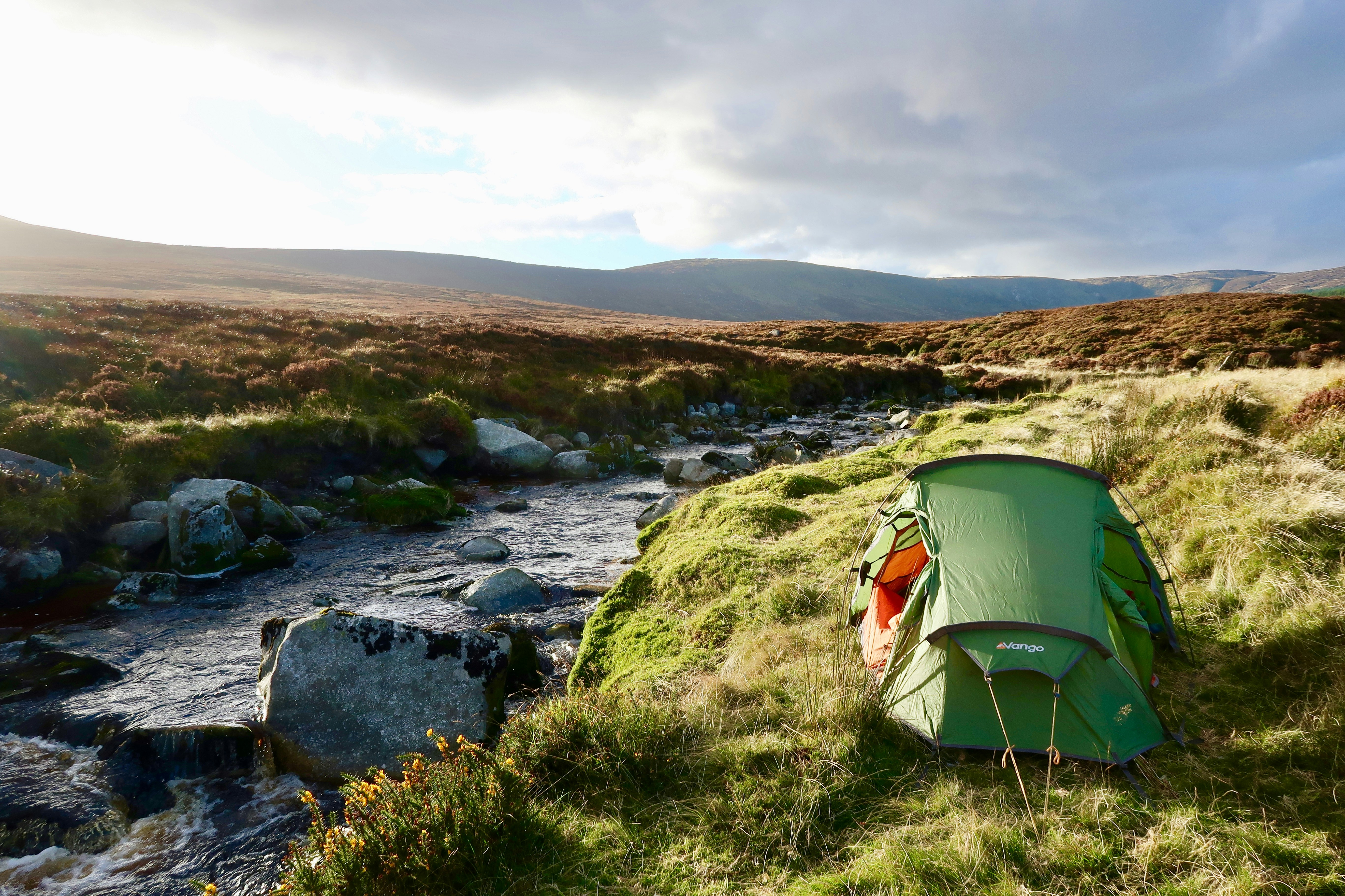 a tent on a grassy hill by a river