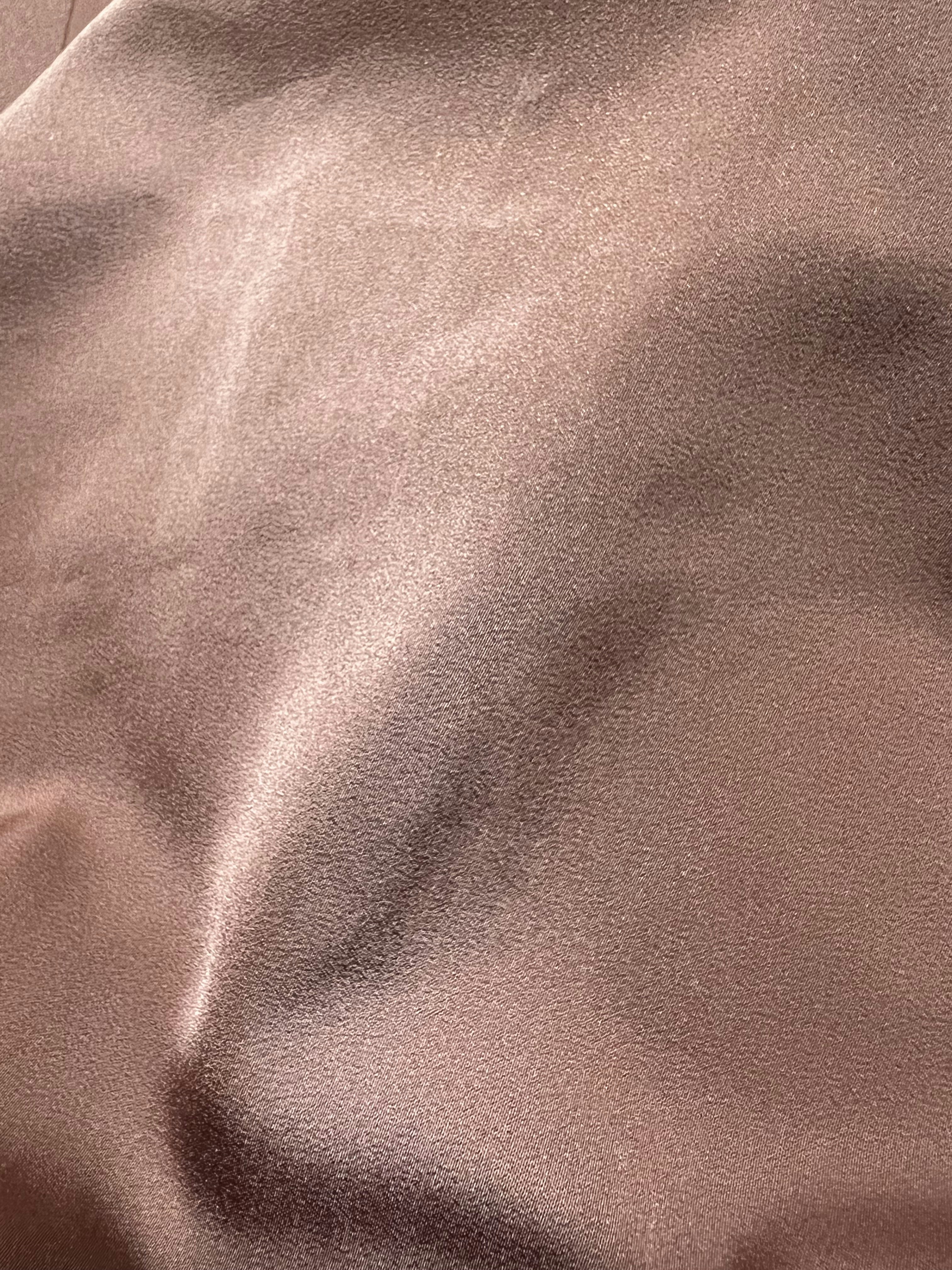 Dusty rose one-piece swimsuit folded on stone surface showing hand-finished seam detail and Italian fabric drape