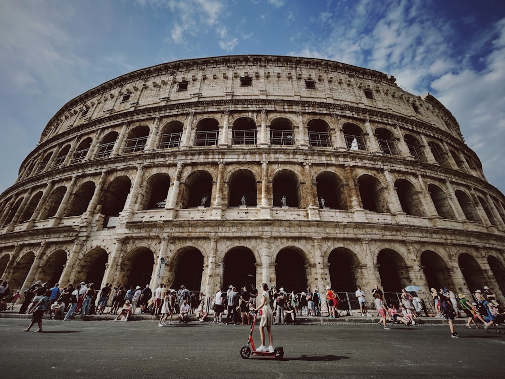 a large circular building with many arches with Colosseum in the background