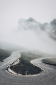 A stark black and white shot of a winding coastal road disappearing into fog.