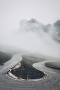Monochrome image of a winding mountain road disappearing into fog.