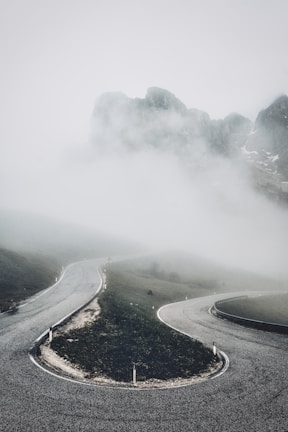A minimalist black and white image of a winding mountain road disappearing into fog.