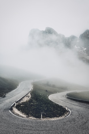 A winding mountain road disappearing into a misty forest at dusk.