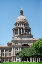 a large building with a flag on top with Texas State Capitol in the background