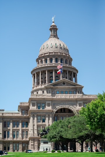 a large building with a flag on top with Texas State Capitol in the background