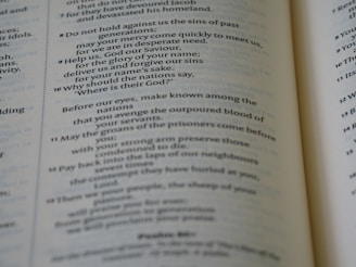 An open book displaying text in columns, with clear emphasis on verse numbers and religious content. The text is aligned in two columns on each page, with some parts italicized for emphasis.