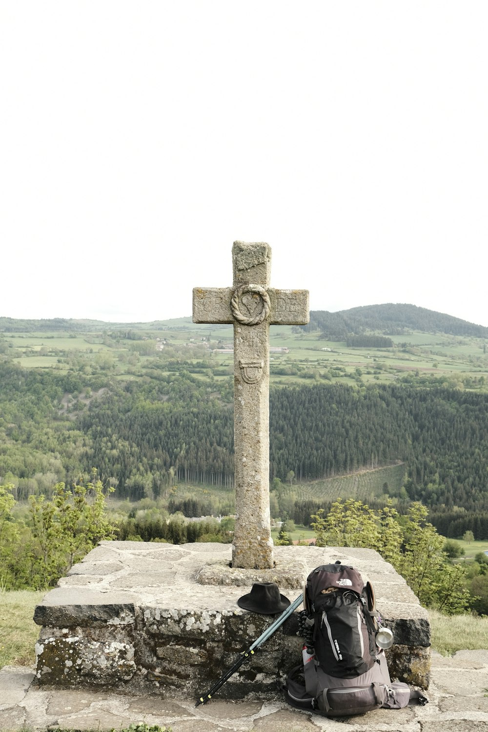 a stone cross with a backpack and a backpack on a hill with trees