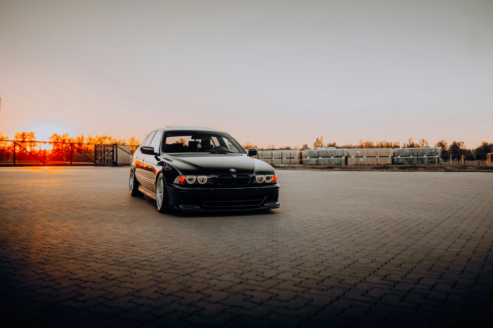 A sleek, comfortable black car waiting outside a bustling airport terminal at sunset.