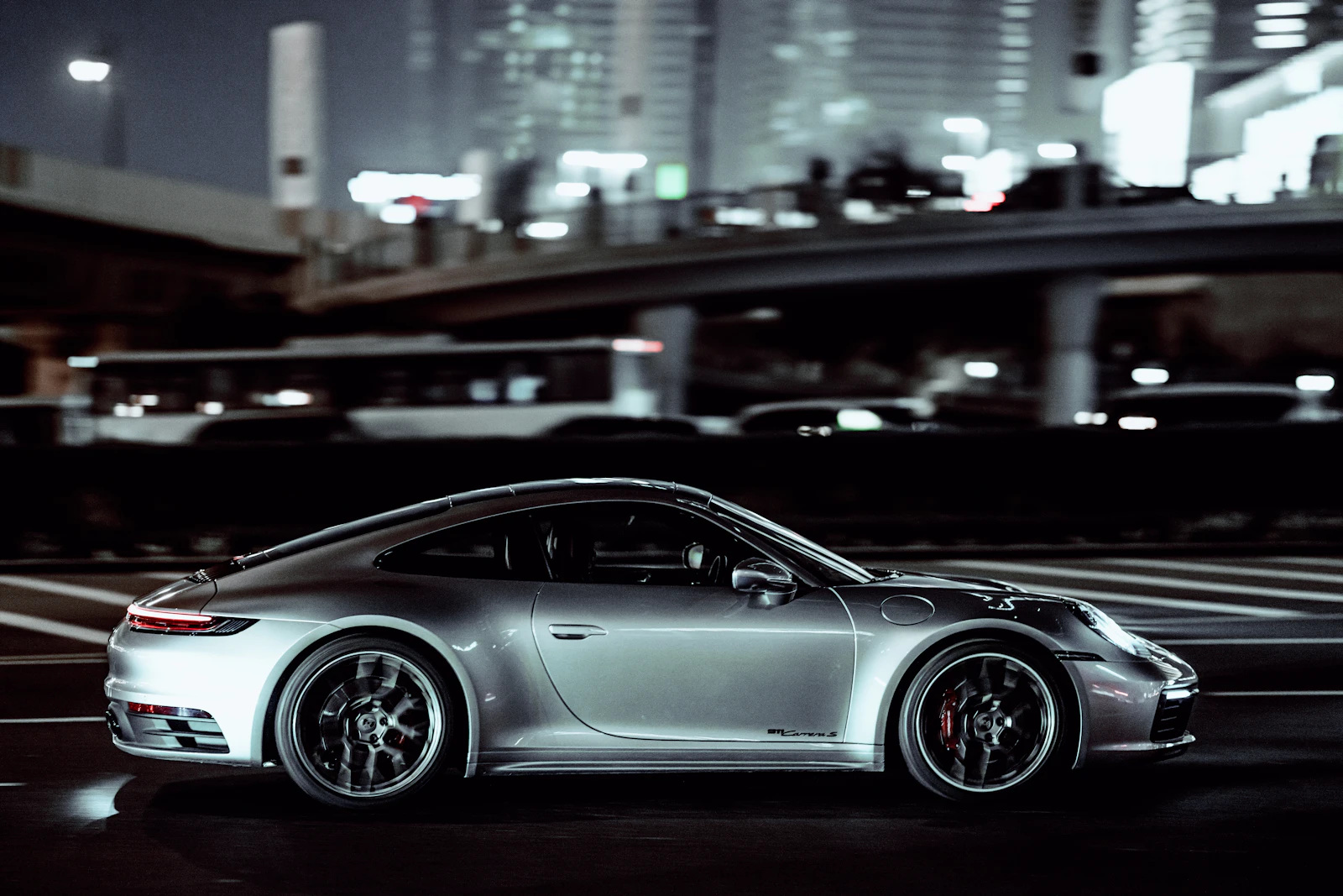 Silver Porsche 911 in side profile on a city street at night