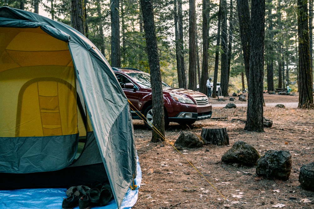 a red car parked next to a tent in a forest