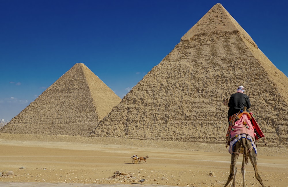a person riding a camel in front of a pyramid