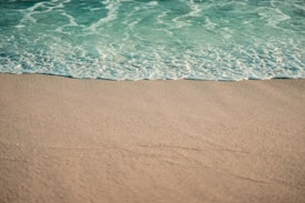 A tranquil beach scene where gentle ocean waves meet the sandy shore under clear weather conditions.