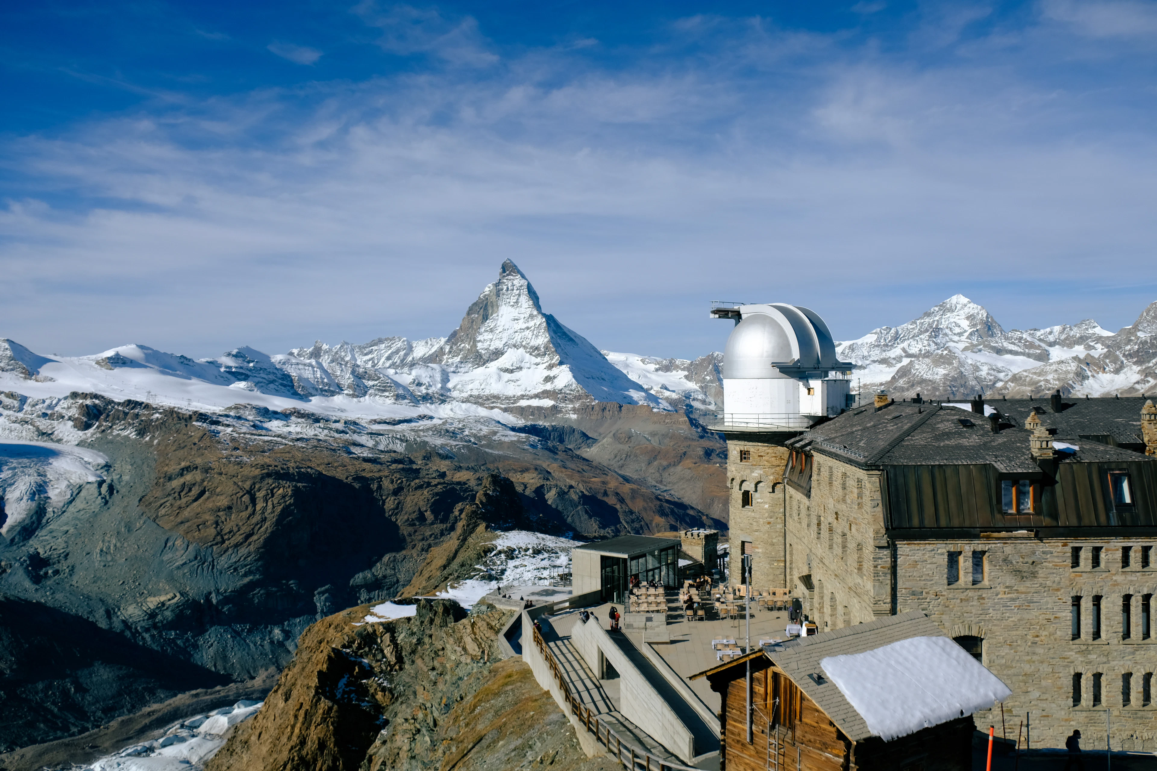 The stone Kulm hotel and its white observatory domes on the Gornergrat summit above Zermatt, with the Matterhorn and a horizon of snow peaks behind them.
