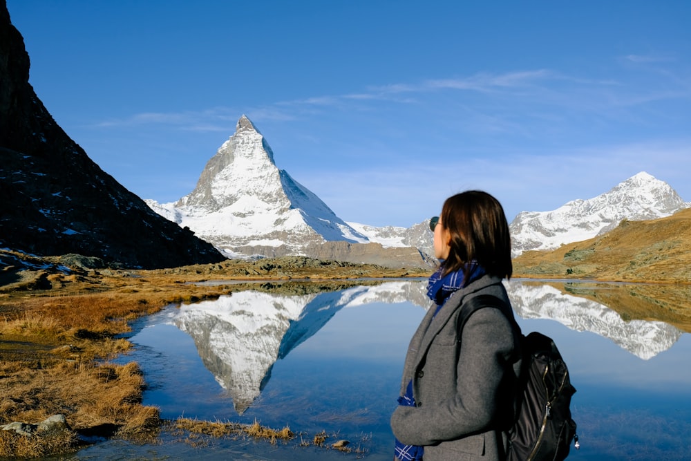 a person standing in front of a lake with snowy mountains in the background