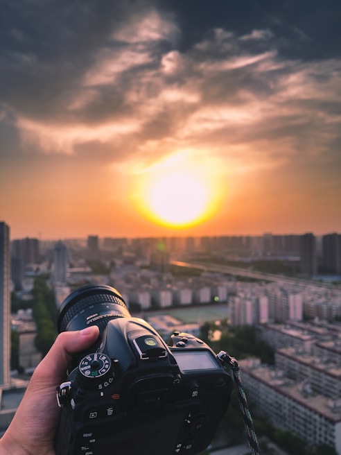 Photographer holding a DSLR camera capturing a sunset outdoors